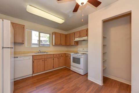 First floor vacant apartment home kitchen with white appliances and hardwood inspired flooring.